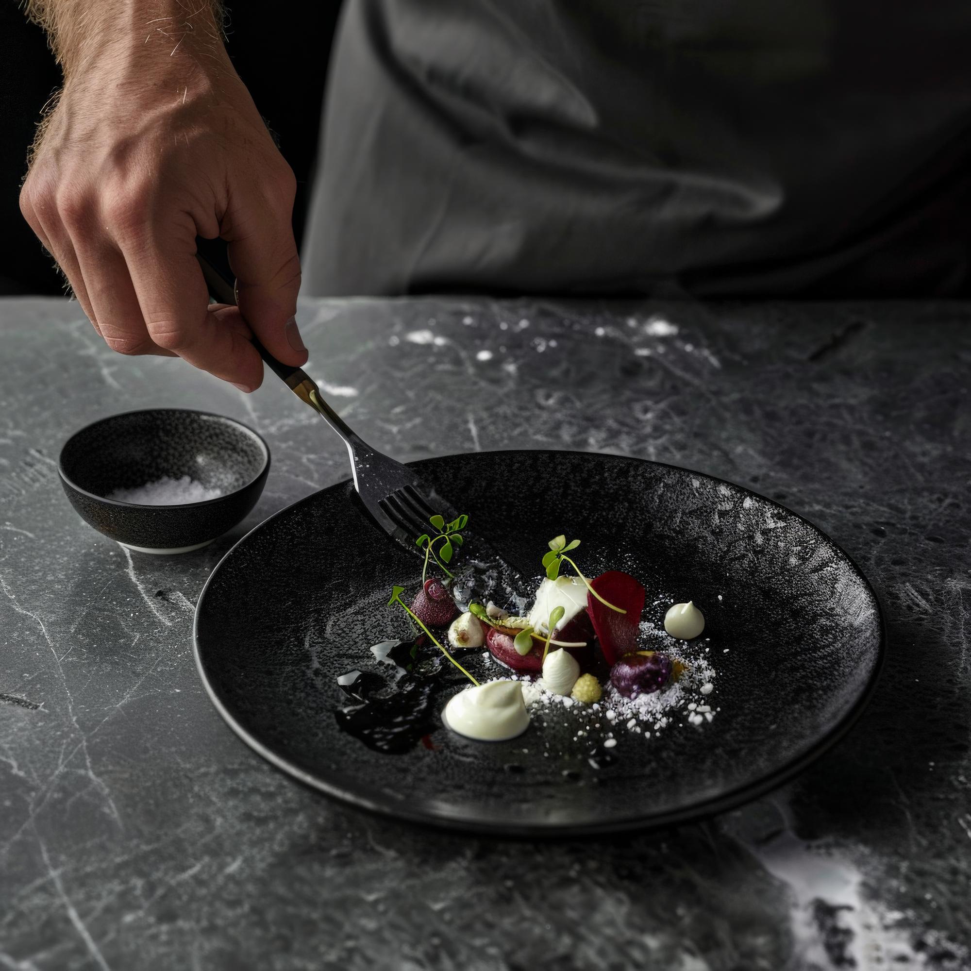 Chef plating a refined dish on a dark plate
